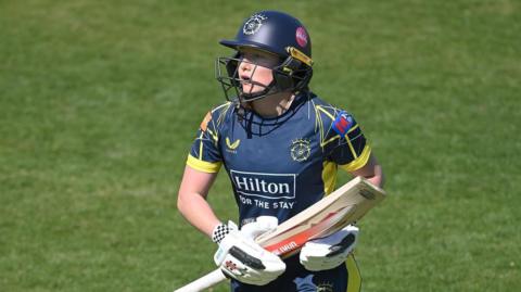 Rhianna Southby holding her bat by the blade and wearing