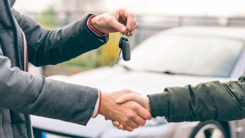 Two people shaking hands, exchanging car keys.