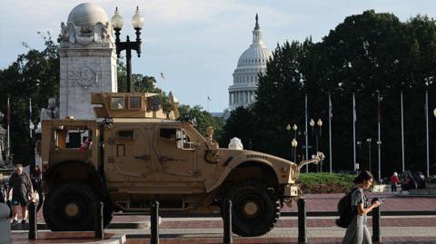 Pedestrians pass an MRAP (Mine Resistant Ambush Protected Vehicles) combat vehicle deployed by the Washington DC National Guard outside Union Station. The US Capitol building is in the distance.