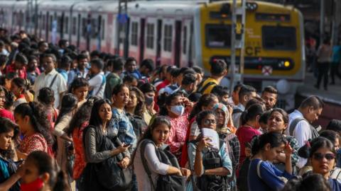 A few dozen people at a rail platform. A train is on the track