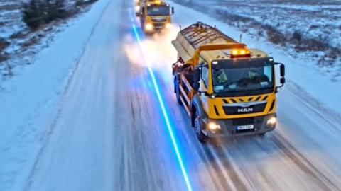 Yellow gritters travelling down a road in Lancashire covered in snow and ice.
