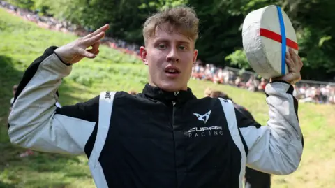 YouTuber Tom Kopke stands posing with his cheese he won at the Gloucestershire cheese rolling race