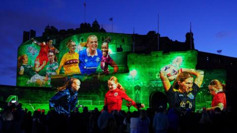 Edinburgh Castle pictured at night lit up in green by a projection of images from Scottish women's football
