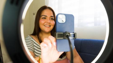 A young woman sets up her phone on a tripod with a ring light around it.