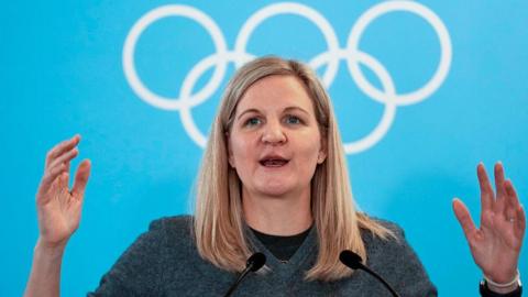 IOC president Kirsty Coventry speaking at the Winter Olympics against a background of the Olympic rings.