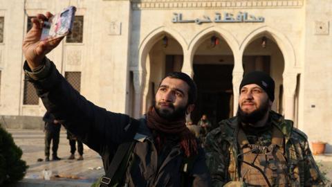 Anti-regime fighters take a 'selfie' picture in front of a government building in Hama, a day after rebels captured the Syrian central-west city, on 6 December 2024