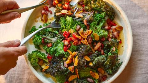 A wide flat white bowl with kale and chilli and almond on a white linen table cloth