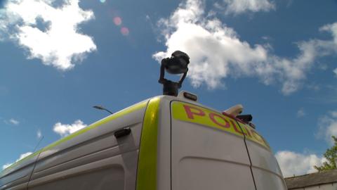 A white police van with cameras and lights attached to the edge of its roof.