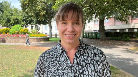 Fiona Vacher standing in a park-like area with trees, flower beds and pathways in the background.