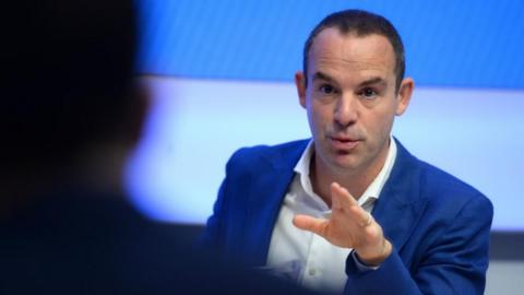 Martin Lewis gestures with his left hand while talking to someone.