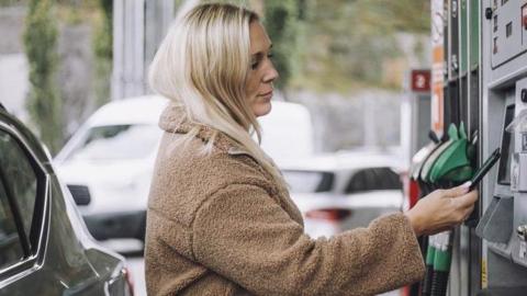 A woman pays for fuel at a pump in a petrol station