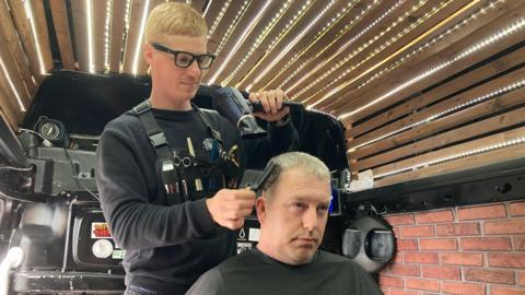 Mr Vorobets combs and blow dries John Edward's hair in his mobile barber van