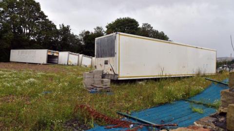 Large, white storage containers and cement blocks in a messy field 