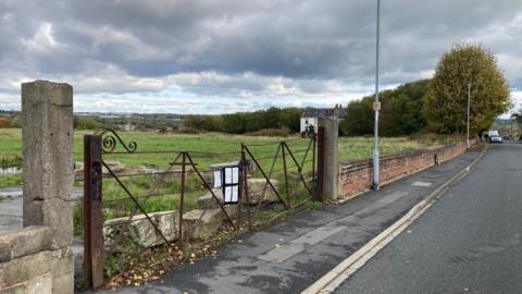 Stone pillars and bent rusting gates at the entrance to the disused quarry site.