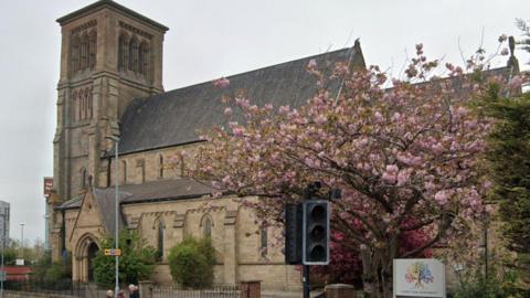 An outside view of St John Church in Darlington with a pink blossom tree on the right next to the building.