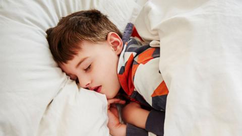 A young boy sleeps in bed.