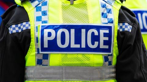 The back of a police officer's yellow high vis vest. It says "Police" in white on a blue strip.