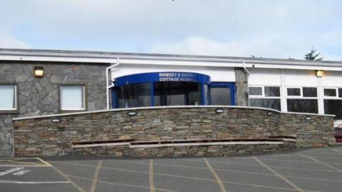 Ramsey Cottage Hospital, a single story building with a brick wall in front of the blue rotating door entance