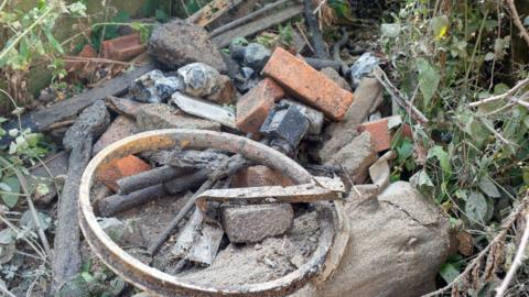 A pile of old broken bricks and lumps of concrete and an old wheelrim.