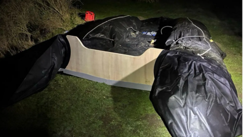 An inflatable boat that was intended for use in a Channel crossing is on an area of grass close to a beach in Belgium.