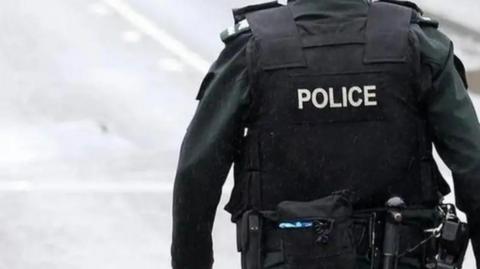 The back of a police officer wearing a black uniform. The world police is written on their back. 