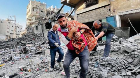 A Palestinian man carries a body in a blanket after an Israeli air strike on a residential building in Beit Lahia, in the northern Gaza Strip (29 October 2024)