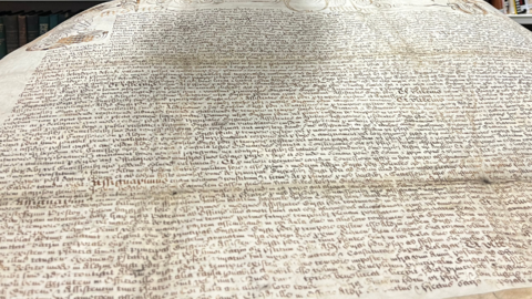 A vellum parchment with small writing on it in latin displayed in Leeds