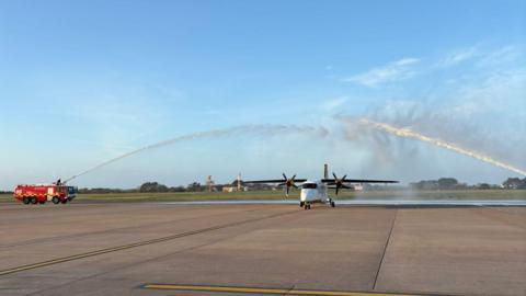 A picture of a plane making its final landing. It is being sprayed with water. 