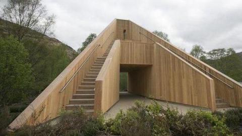A large wooden tower, shaped like a pyramid, sitting near a loch