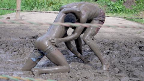 Two men covered in mud wrestle in a ring