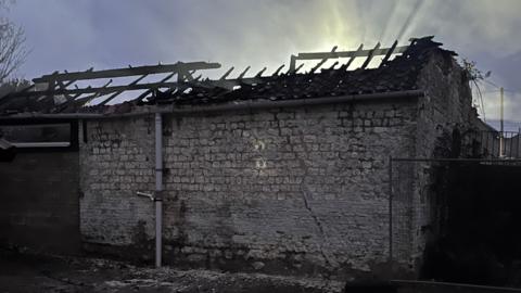 A stone barn with the burnt out embers of a wooden roof on display. 