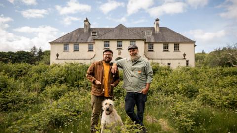 Banjo Beale and his husband Ro standing outside a crumbling mansion