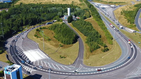 Aerial shot of the northbound Tyne Tunnel with cars and lorries exiting. There are patches of grass and trees nearby. 