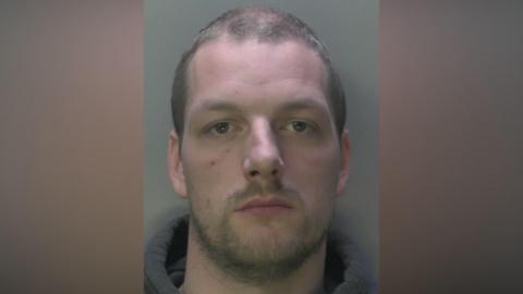 A police mugshot of Dion Arnold, a man with short brown hair in a grey hoodie.