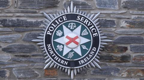 A large PSNI crest, displaying the Police Service of Northern Ireland, on a grey stone wall.
