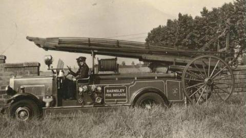 A sepia photograph of an old fire engine. A sign on its side reads "Barnsley Fire Brigade".