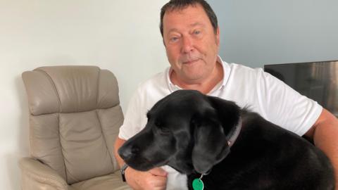A man with a black labrador in a living room