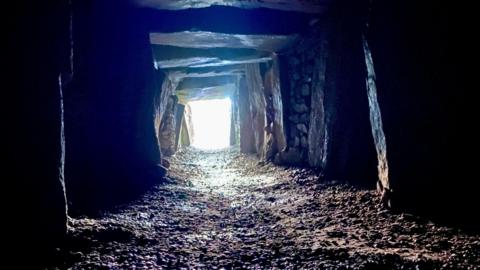 The passage grave at La Hougue Bie is rectangular in shape and made of stone. It leads to daylight.