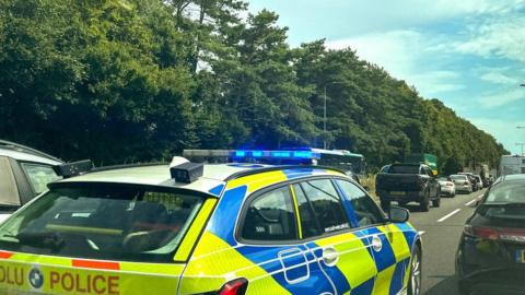 Close up of police car travelling down a motorway. There are other cars and lorries in the background.