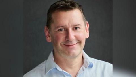 A man looks at the camera wearing a blue shirt.
