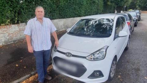 A man stands by a white parked car