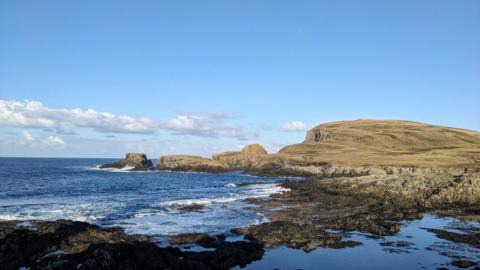 Blue sky above the blue sea inlet with a rocky mountain inbetween