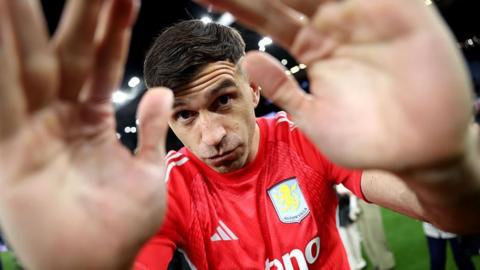 A close up image of Aston Villa's Emiliano Martinez putting his hands partly over the camera