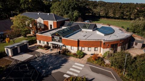 An aerial shot of a circular building with trees and fields in the background.