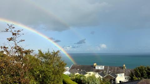 A double rainbow in a grey-blue sky seen over coastal houses