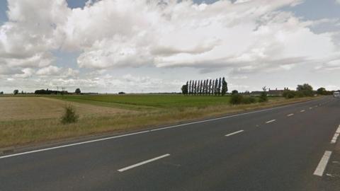 Part of the A47 between Thorney and Eye in Cambridgeshire. The surrounding landscape is flat and there are fields and trees in the background