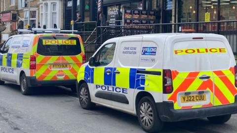 White police vehicles with blue, orange and yellow markings parked outside shops and houses