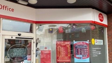 Post Office window with cream and red signage and posters