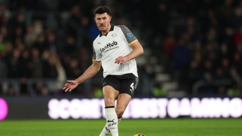 Danny Batth, wearing Derby County's white and black home kit, playing football during the side's match against West Bromwich Albion in January
