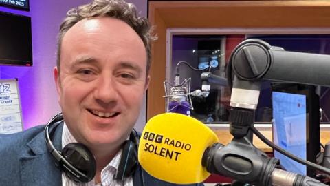 Danny Chambers smiling in front of a BBC Radio Solent microphone